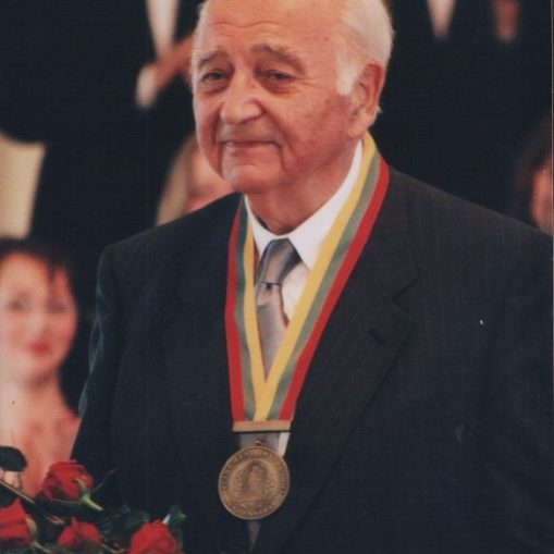 Vyras su ordinu ant kaklo ir raudonų rožių puokšte rankose.