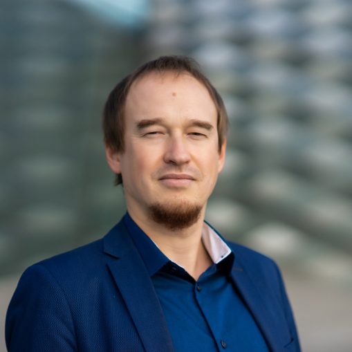 Vyras su mėlynu švarku ir marškiniais, su barzdele, žiūri tiesiai į kamerą.