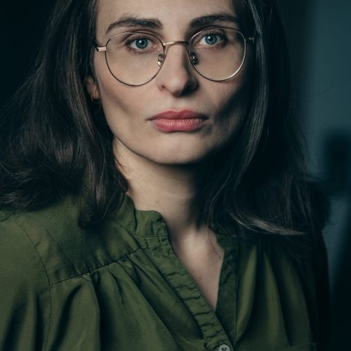 Portretas arti moters veido su akiniais ir žalios spalvos marškiniais.