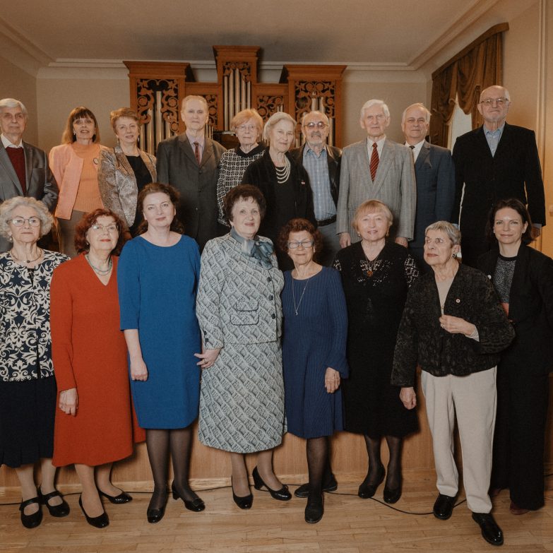 Grupė senjorų pozavo nuotraukai, stovėdama ant pakylos priešais vargonus ir užuolaidas.