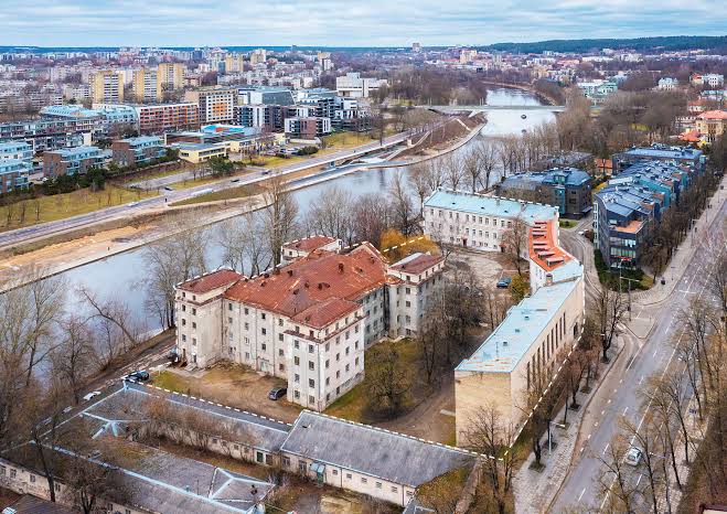 Gatvės ir pastatų vaizdas iš oro su upe, pėsčiųjų taku ir keliais.