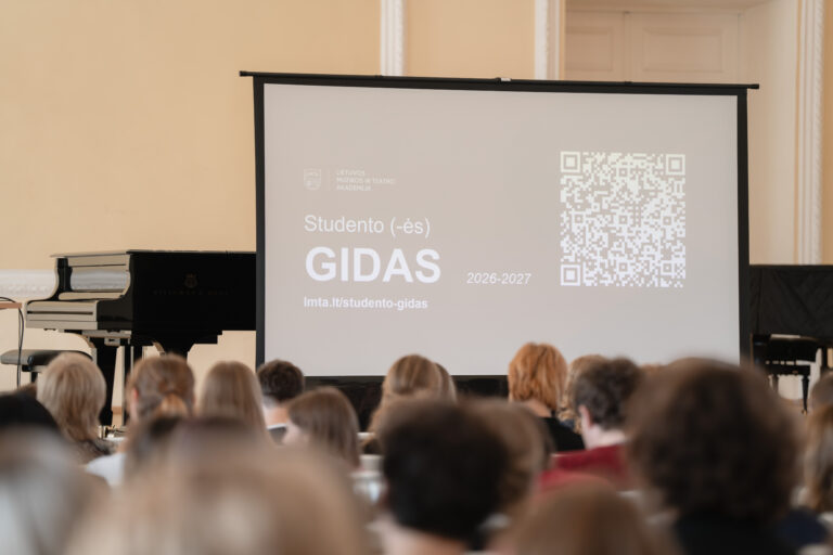 Juodas pianinas ir ekranas su studento gido informacija ir QR kodu, priešais žiūrovų grupę.