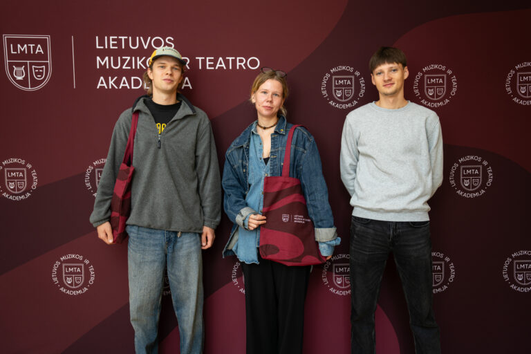 Trys jaunų žmonių grupinė nuotrauka ant tamsiai raudono fono su LMTA logotipu.