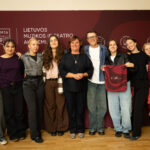 Grupė žmonių, tarp jų moteris ir kelios merginos bei vienas vaikinas, stovi prieš tamsiai raudoną foną su LMTA logotipais ir užrašu „LIETUVOS MUZIKOS IR TEATRO AKADEMIJA“. Nuotrauka daryta horizontaliai, žmonės šypsosi.