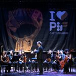 Styginių orkestras su dirigentu ir akordeonistu scenoje priešais „I Love PIF Castelfidardo“ reklamjuostę.